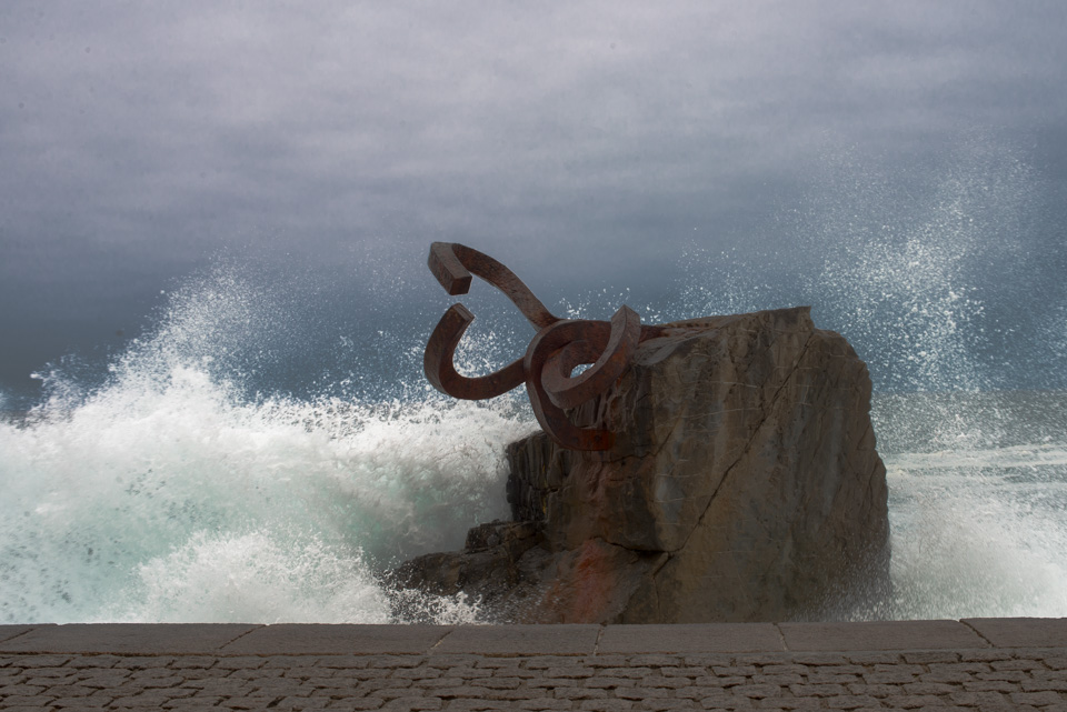 waves crashing around the rock, next to an ocean sculpture