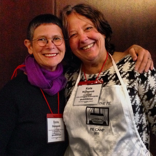 two women standing together while one of them is wearing a white apron