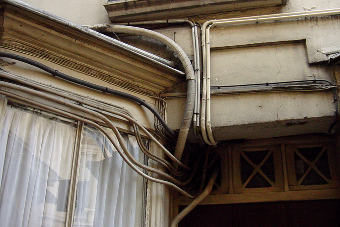 an up - and - down image of a wall made of pipes, wires, and windows