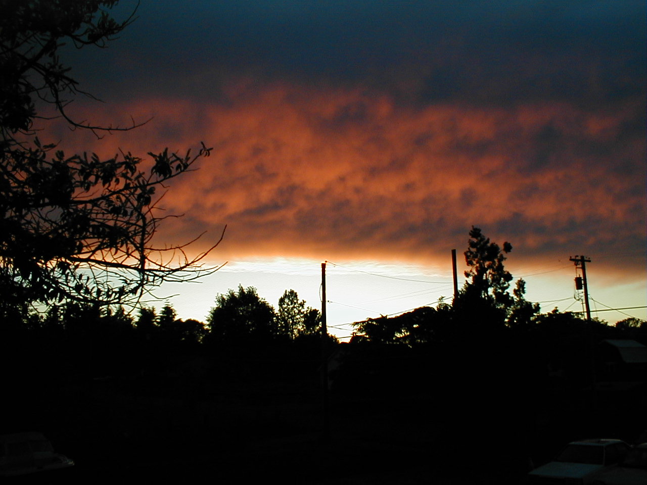 the sun sets behind clouds in the sky over trees