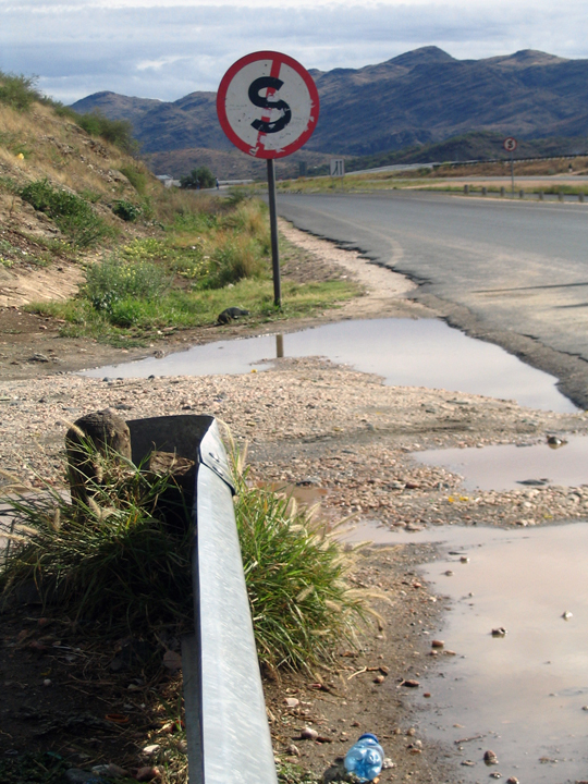 a red sign sitting above a dle of water on the side of the road