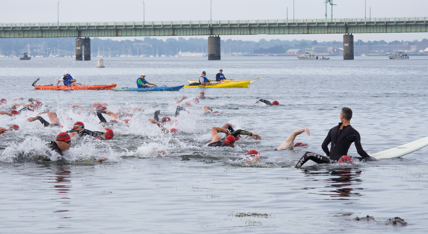 swimmers paddling into a large body of water under a bridge