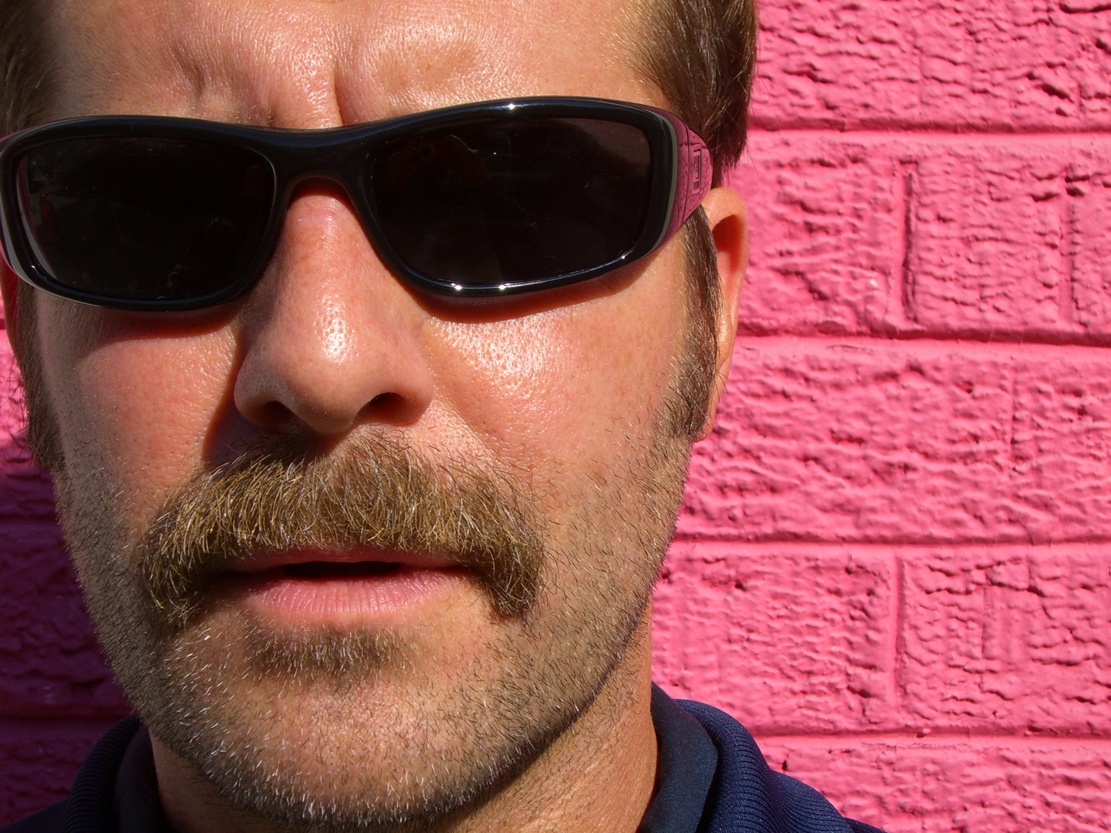 a bearded man with sunglasses on in front of a wall