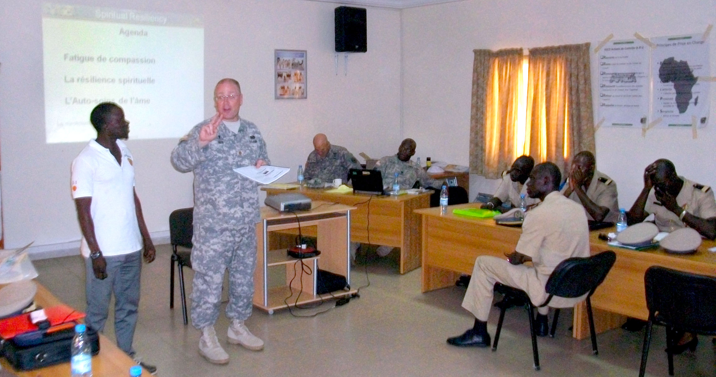 man in fatigues standing up speaking to military members