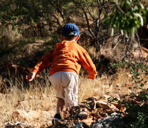 small boy wearing orange jacket running up a path