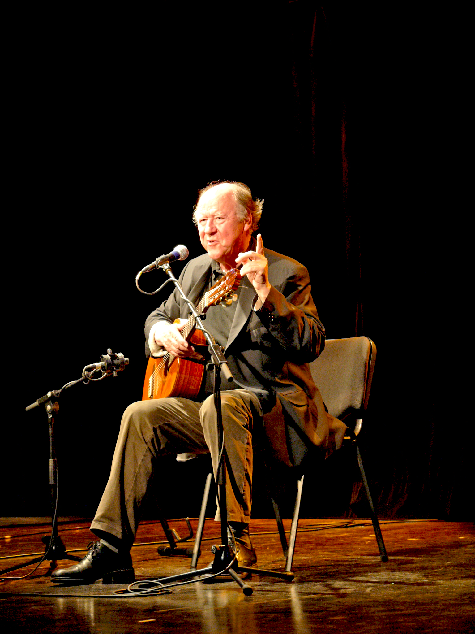 an old man playing on a guitar in front of microphones