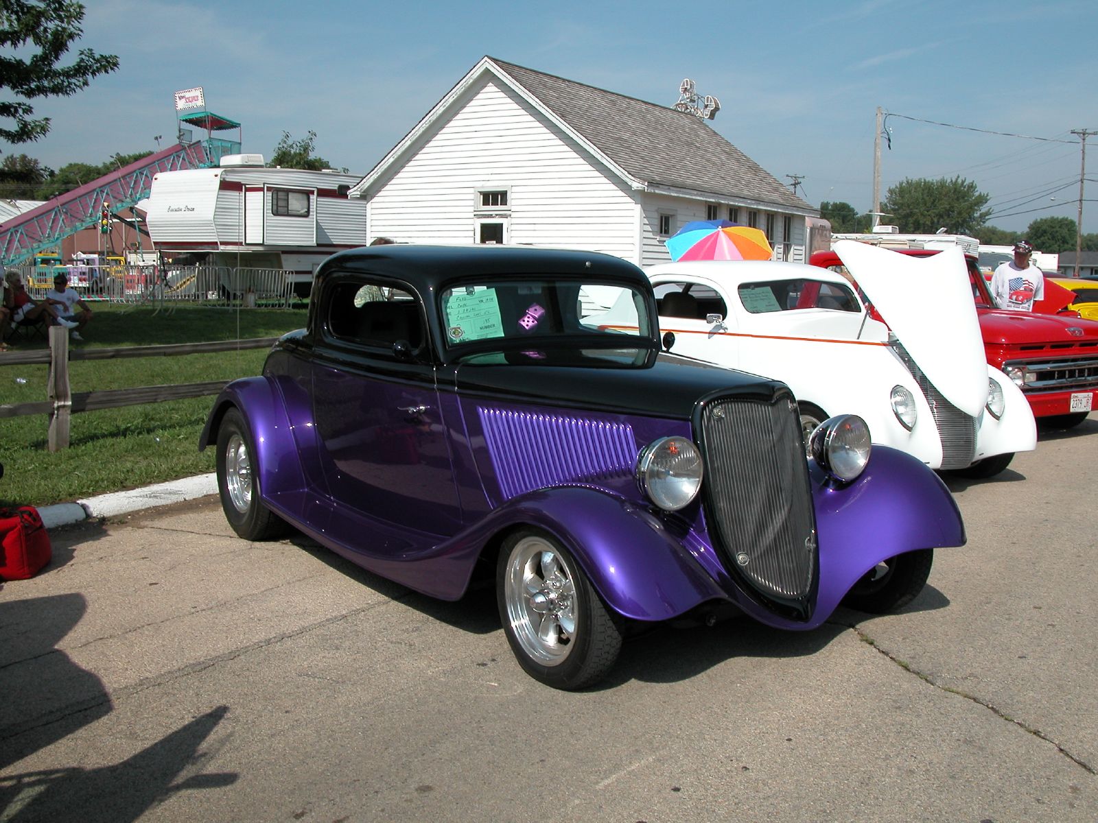 two old style  rod cars sit parked next to each other in front of a house