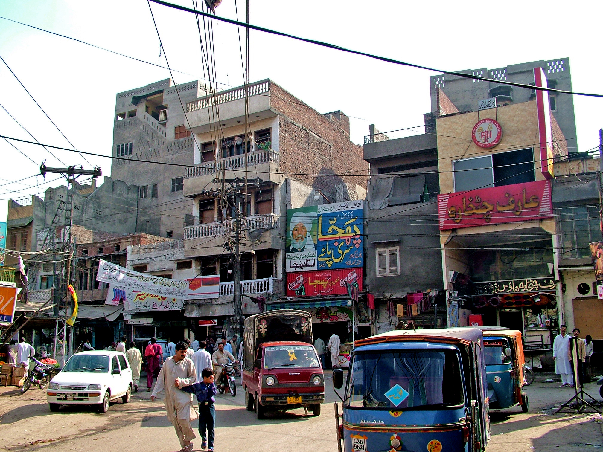 several people on street corner near vehicles with buildings in background