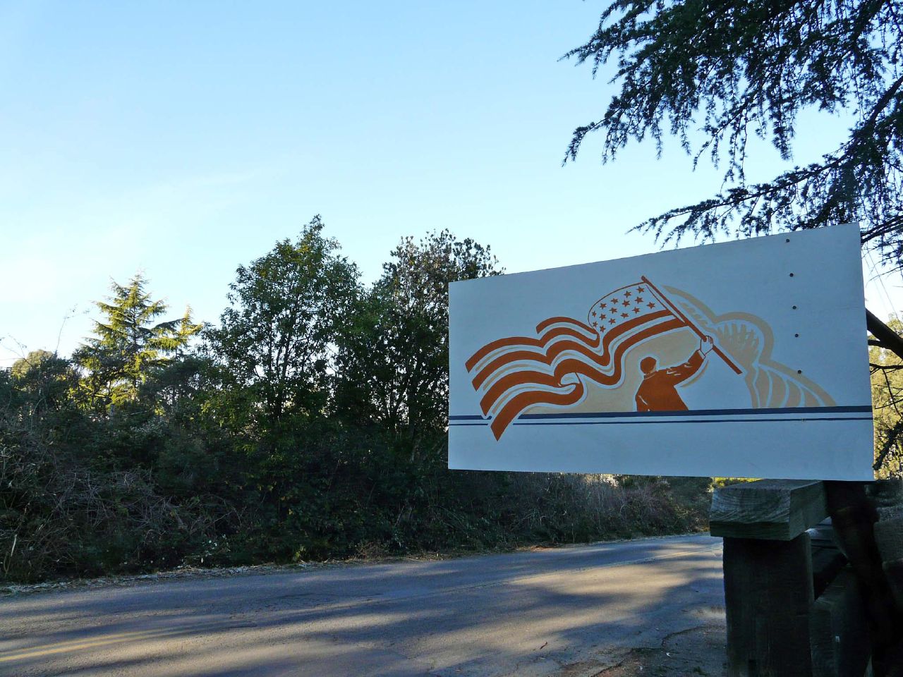 a sign with an american flag on it by the side of the road