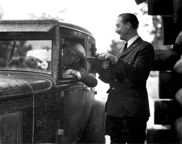 a man holding soing in his hand and standing next to an old car