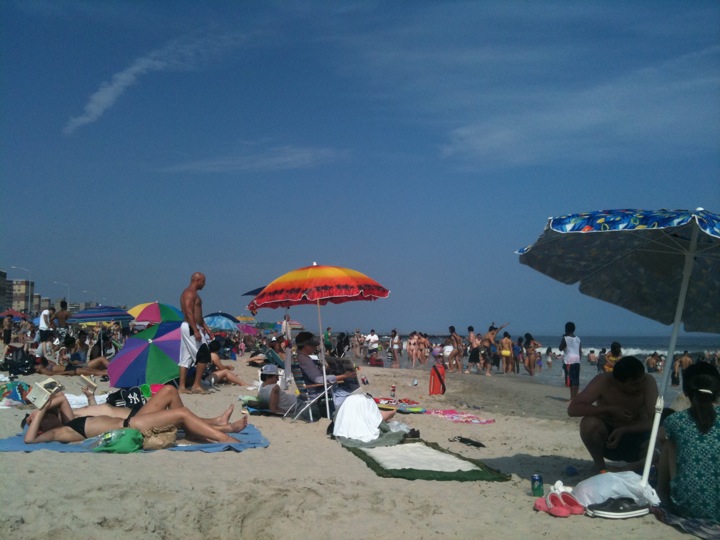 beach goers sit beneath umbrellas on the sandy beach