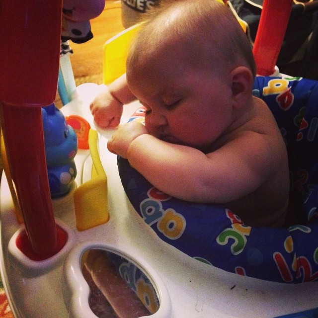 a baby in a fisher's baby bouncer with his head down