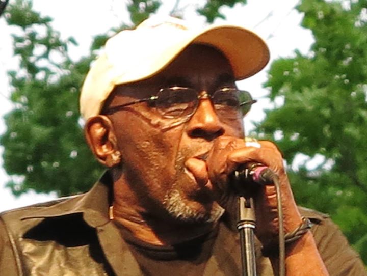 a man wearing glasses and a hat speaking into a microphone