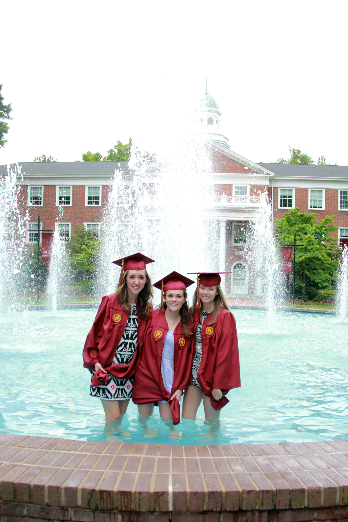 four students in graduation robes pose near a fountain