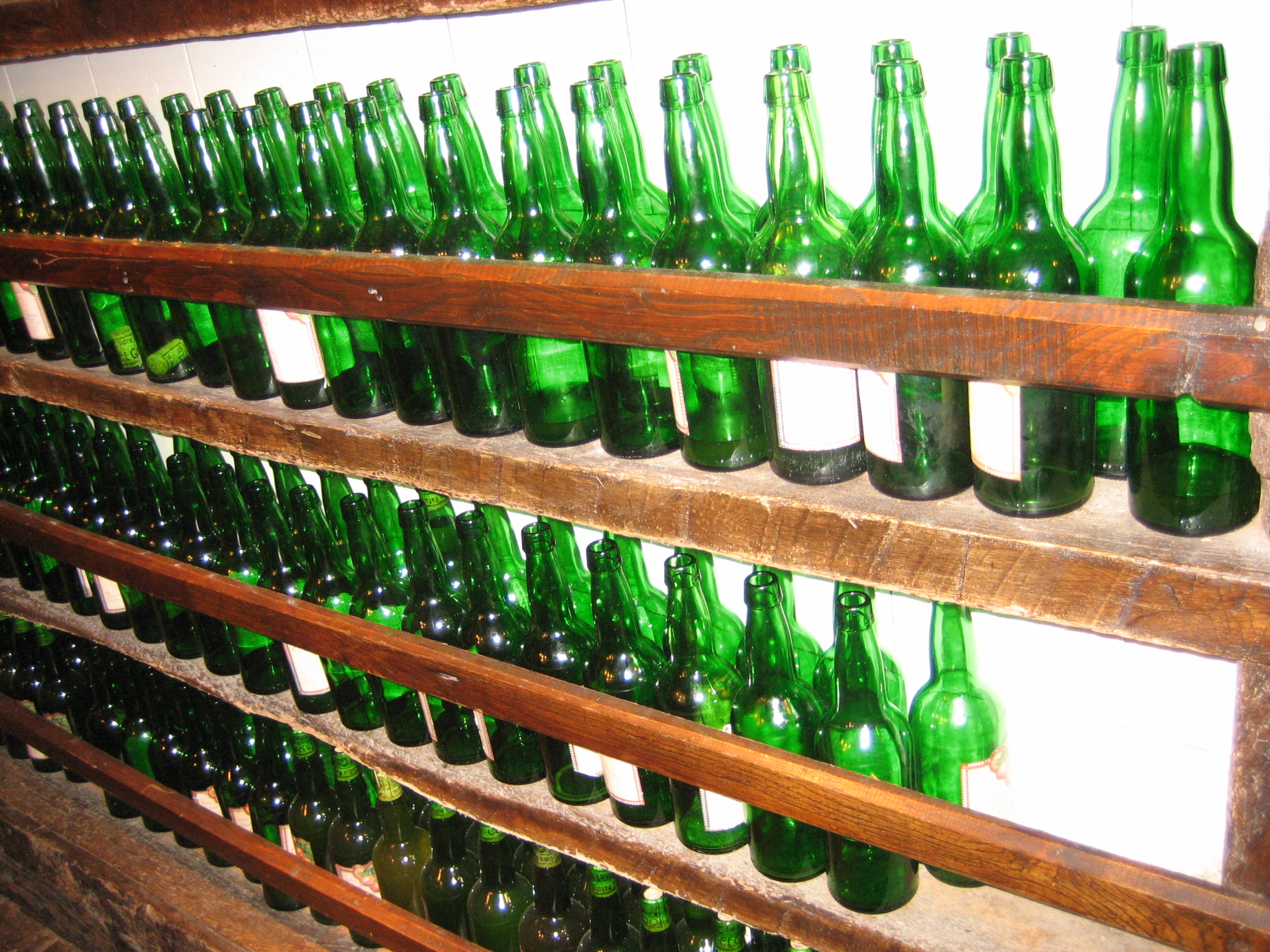 a wooden shelf with many empty green beer bottles