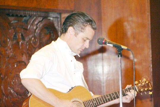 a man standing in front of a microphone playing an acoustic guitar
