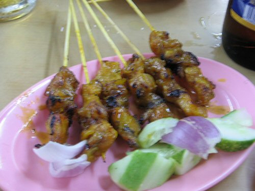 a pink plate topped with satay and vegetables