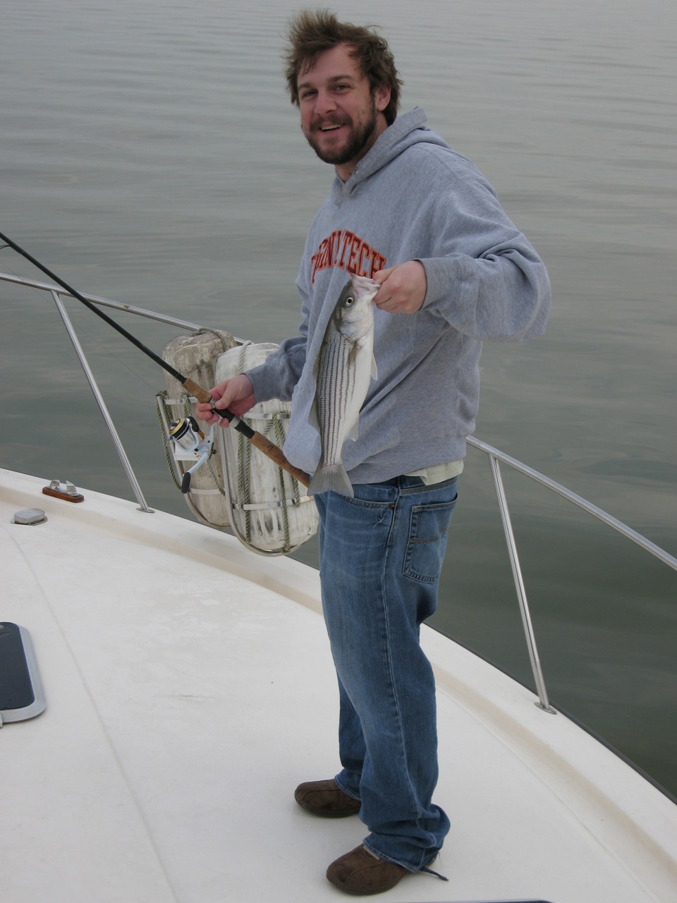 a man in grey shirt holding a fish on a boat