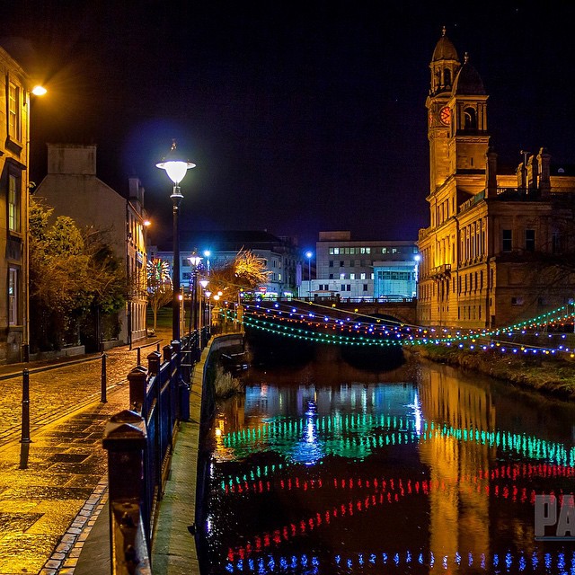 a light up walkway leading to a clock tower over a city river