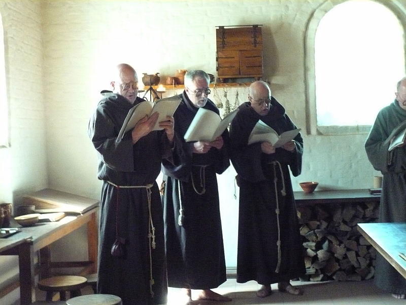three men in black robes are in a large room with wooden tables