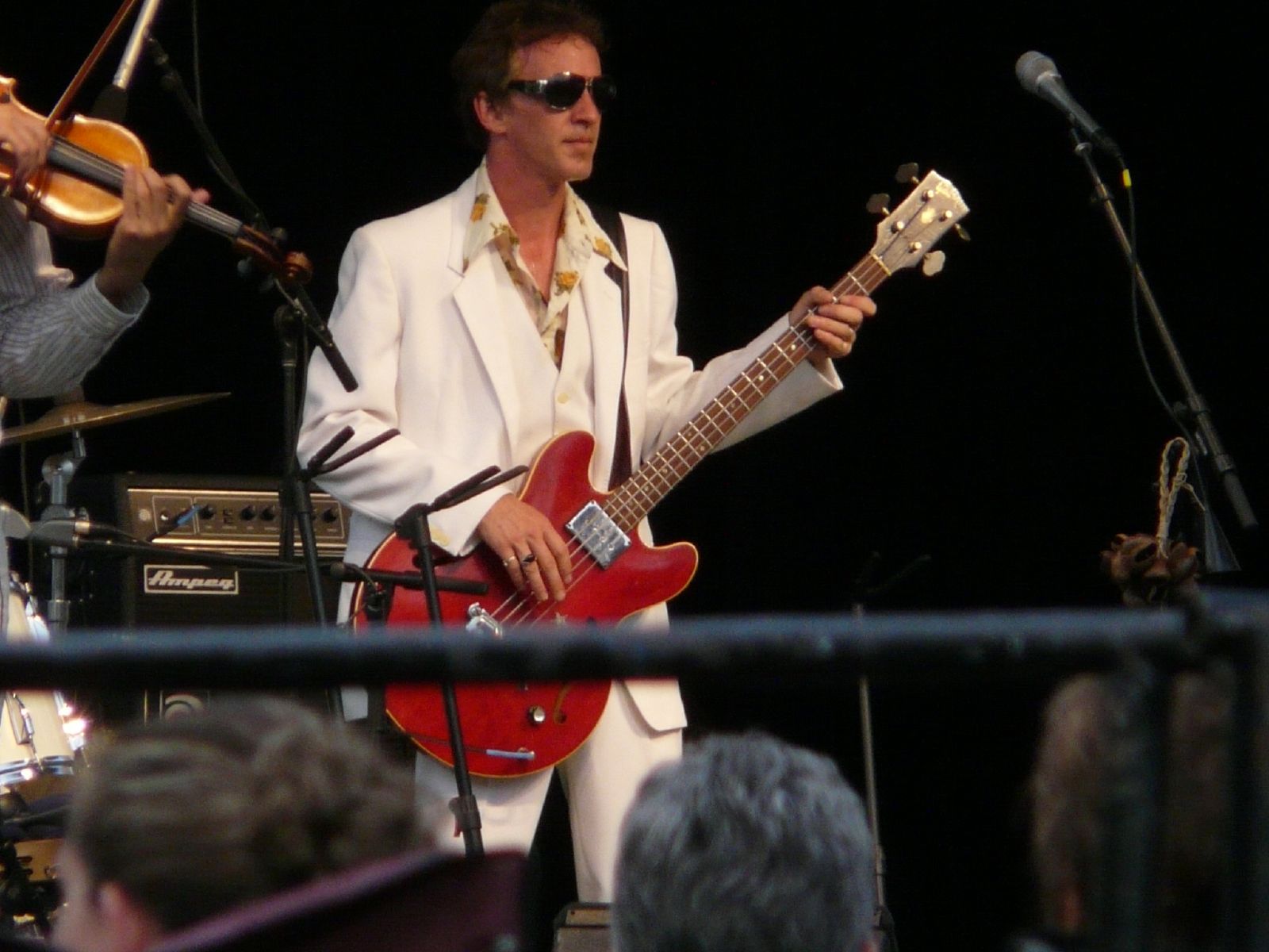 a man in a white suit and sunglasses playing an electric guitar