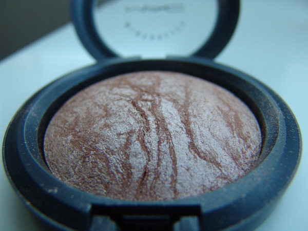 a powdered eyehadow sits inside an open compact, black - rimmed case