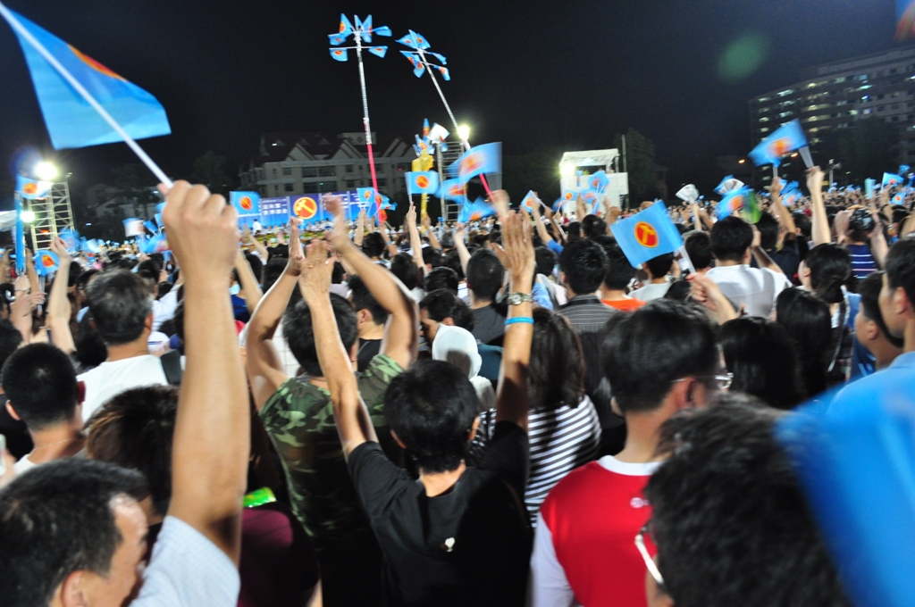 crowd of people raising flags on night with lights and signs