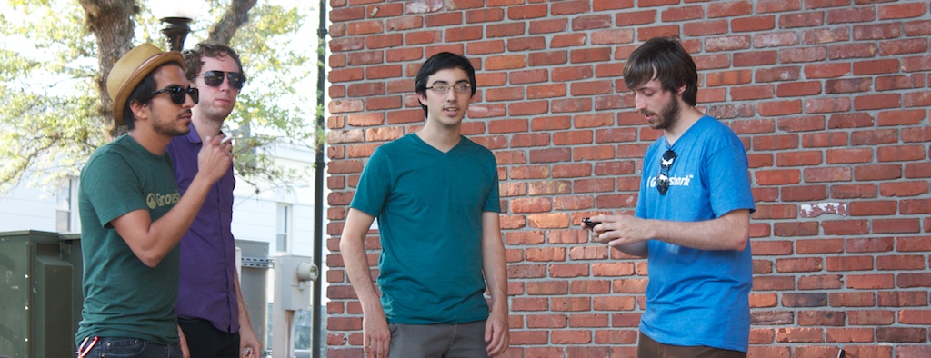 three guys standing near a brick wall texting on their cell phones