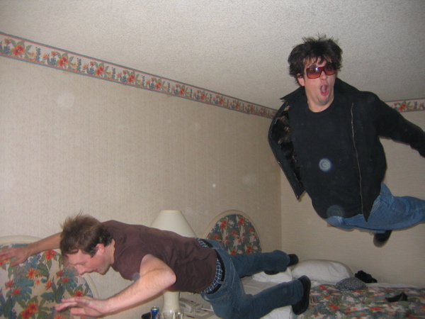 two men are jumping up on bed beds and a lamp