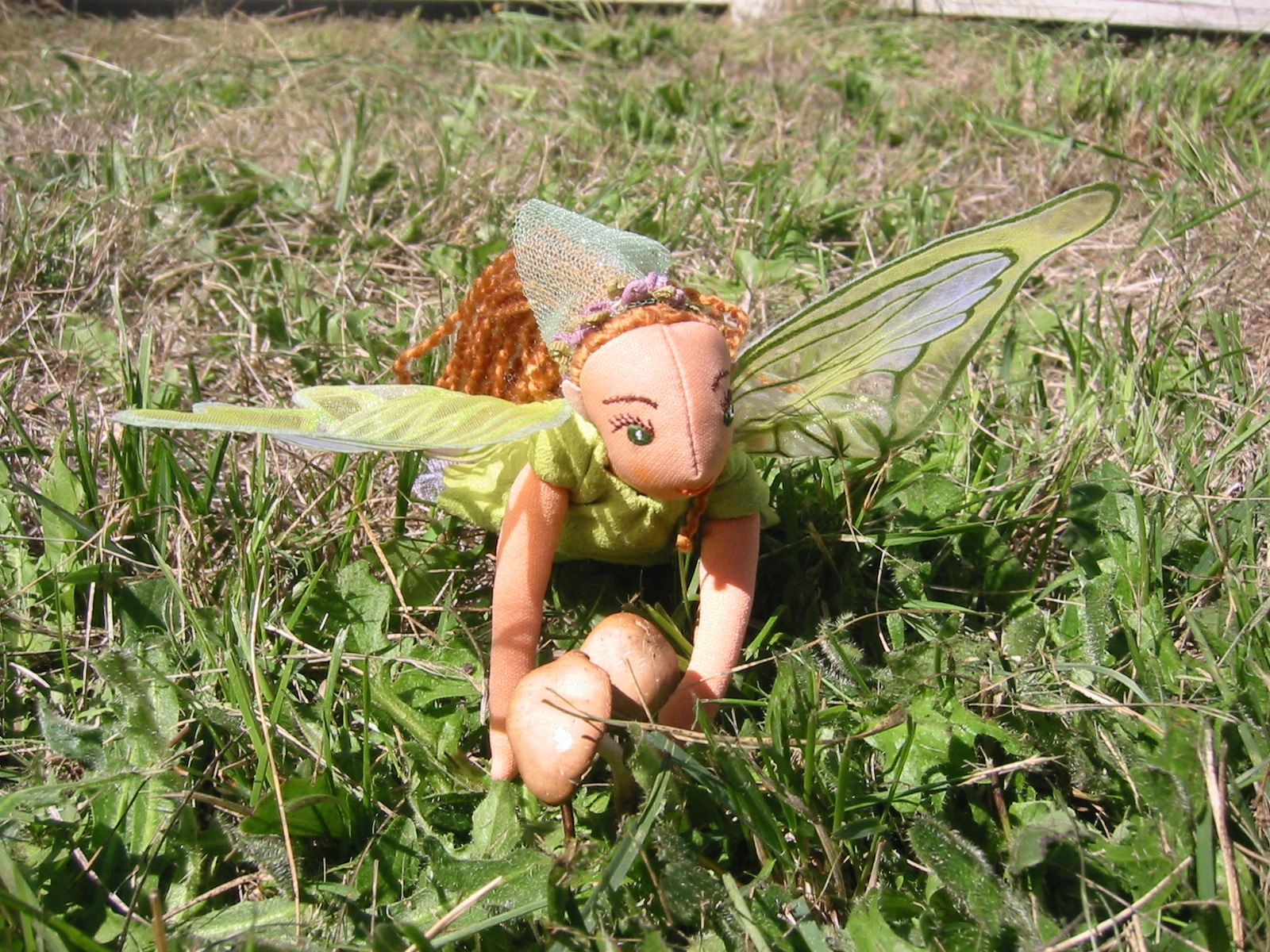 the green fairy doll sits in grass and looks like it is looking around