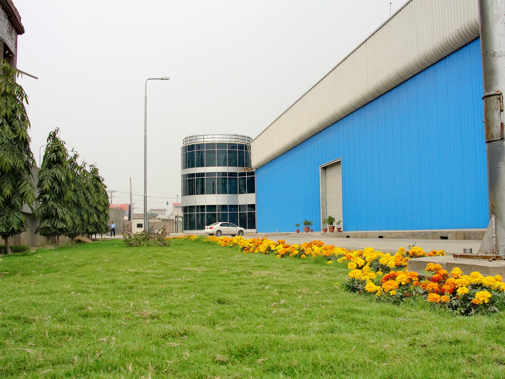 yellow flowers grow beside the grass in front of an industrial building