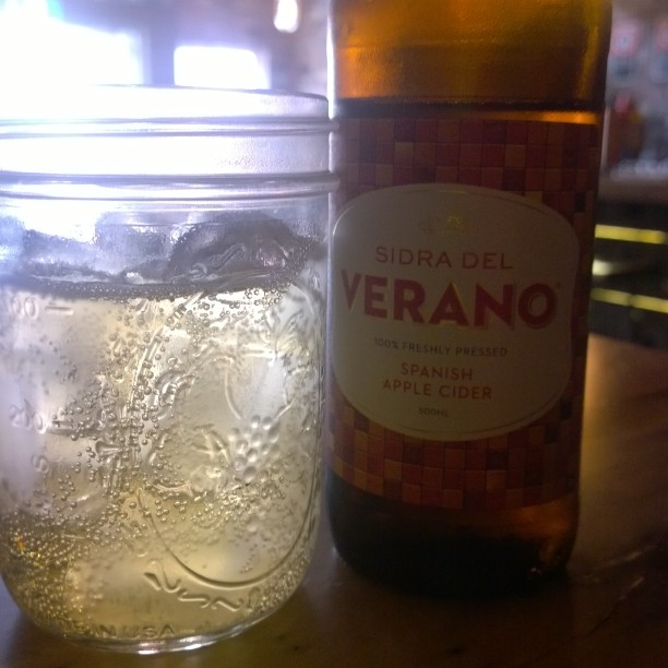 a jar with some water inside of it sitting next to a bottle of beer