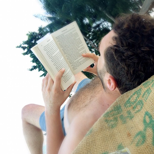 a shirtless man reading a book on a bench