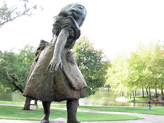 statue of a woman carrying a bag in a park