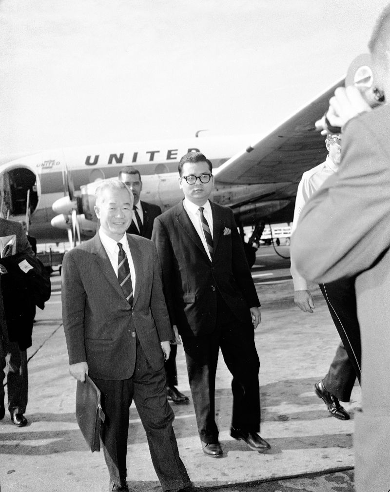 two men in suits standing in front of an airplane