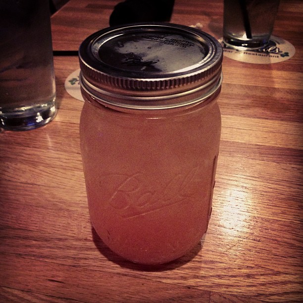 a mason jar sitting on top of a wooden table next to two glass cups
