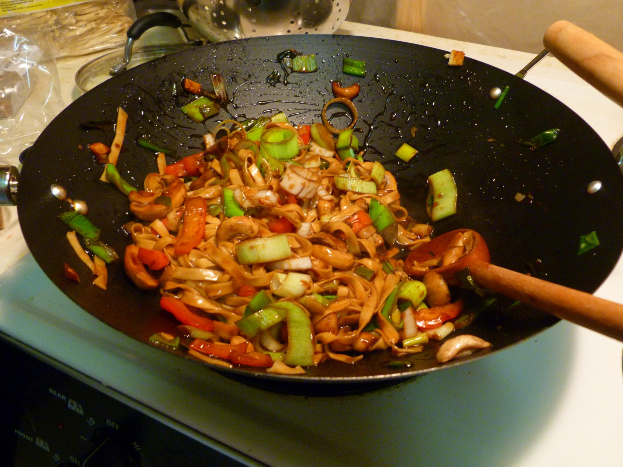 asian food being cooked in a wok on a kitchen stove