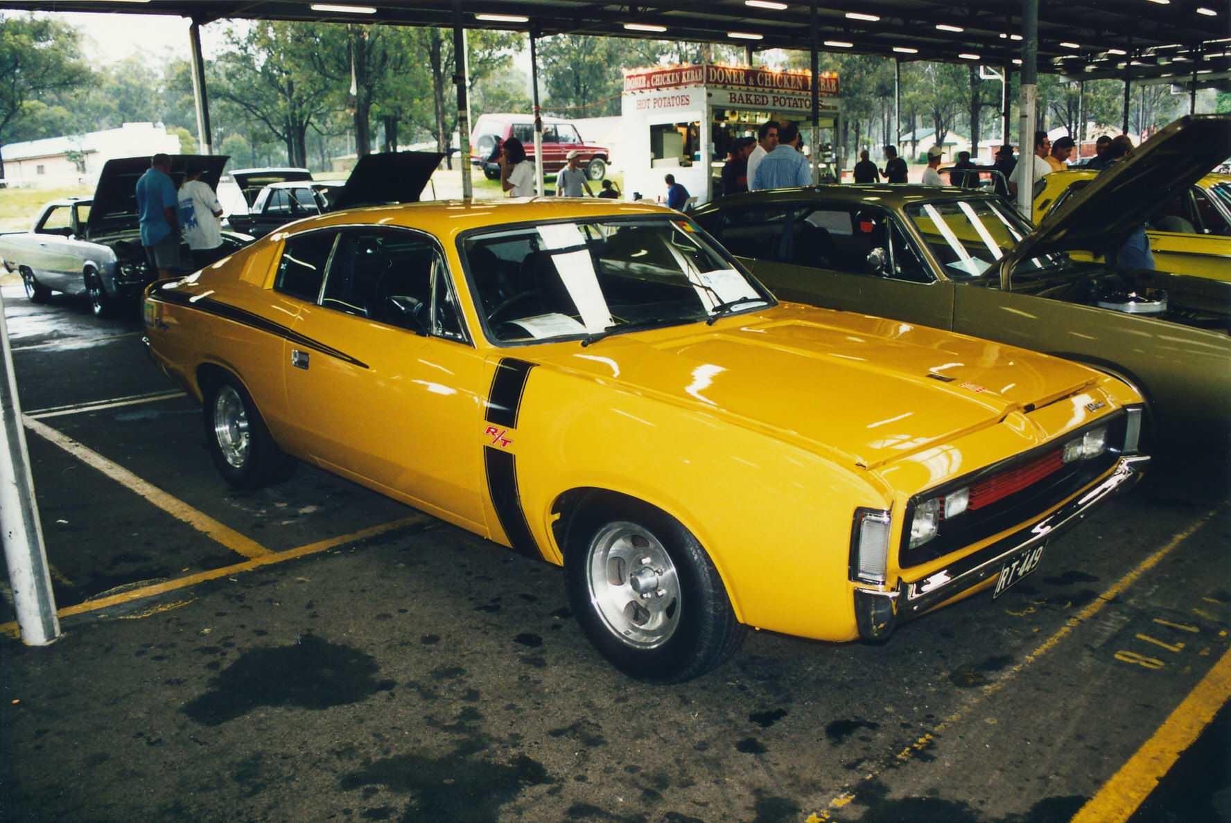 a car show with two yellow cars in the foreground and people looking