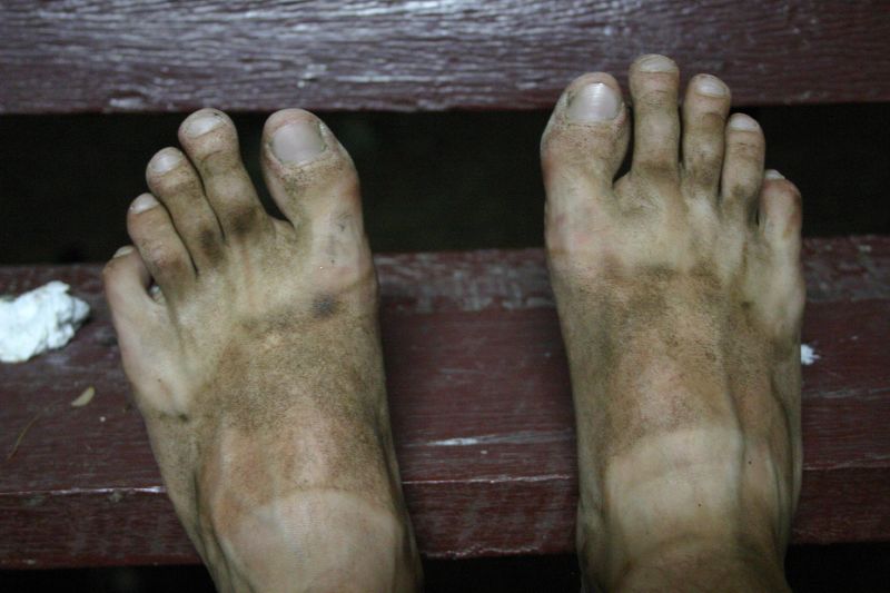 a person with dirt on their feet has a piece of plastic in his mouth