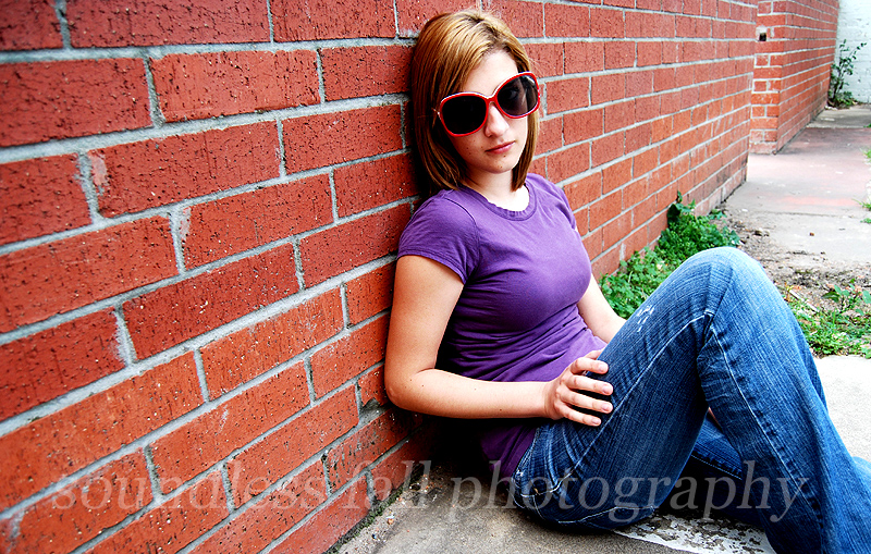 wearing sunglasses leaning against red brick wall
