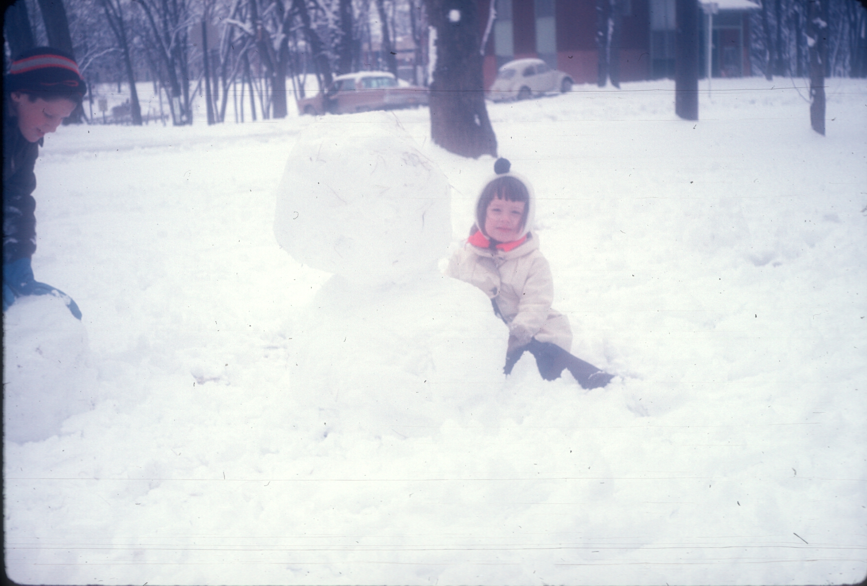 a little  playing in the snow next to a snowman