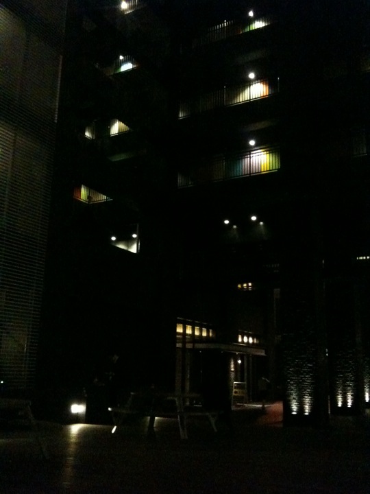 an illuminated building in the dark with a table and chairs