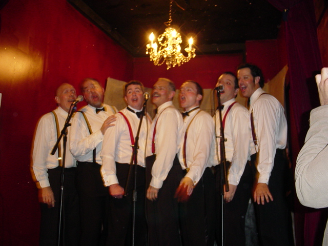 several men with ties that are singing in front of people