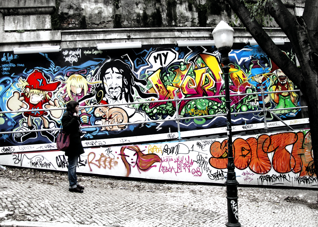 a woman is walking by an outside wall that has colorful graffiti