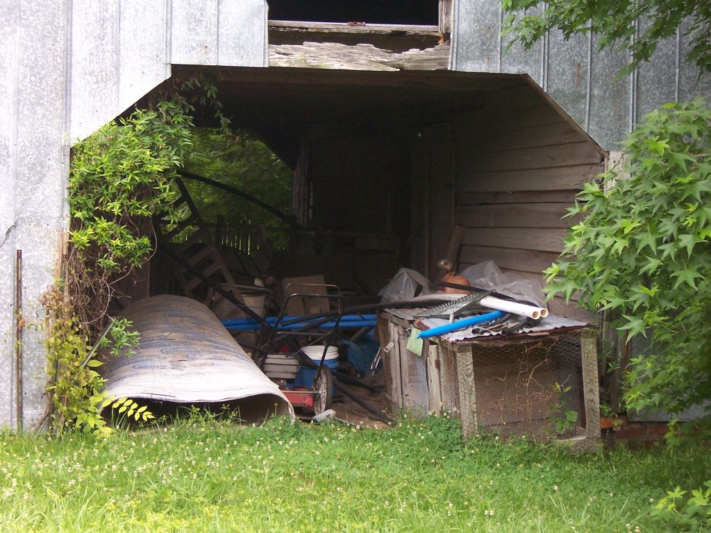 a boat lying outside on the grass by an old barn