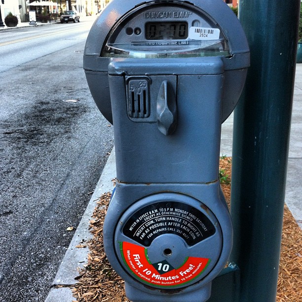 a coin operated parking meter next to a green pole on a street corner