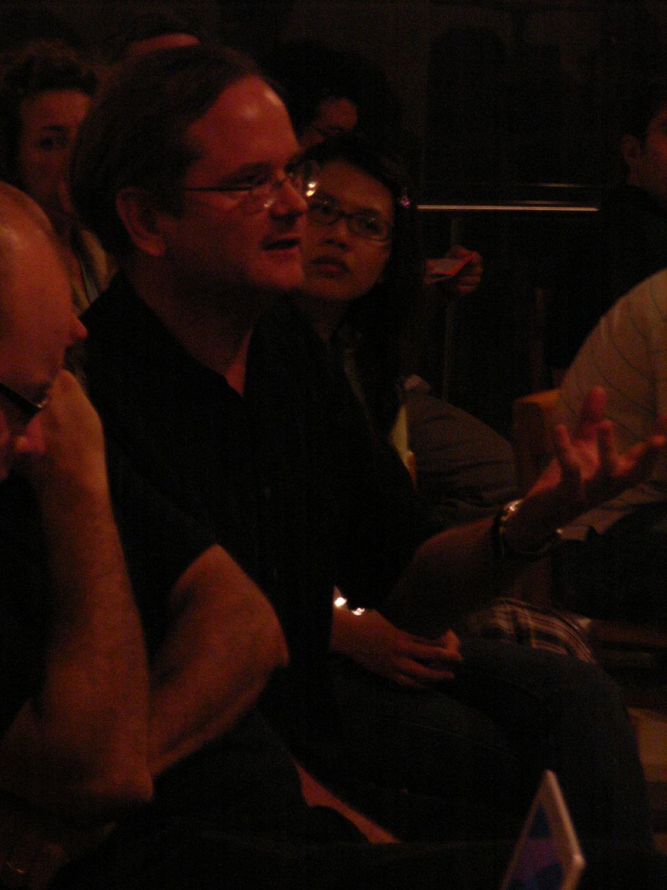 a man with glasses sitting on a chair with other people