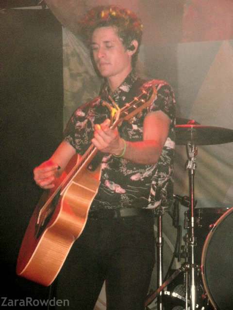 the young man is playing his guitar while standing on stage