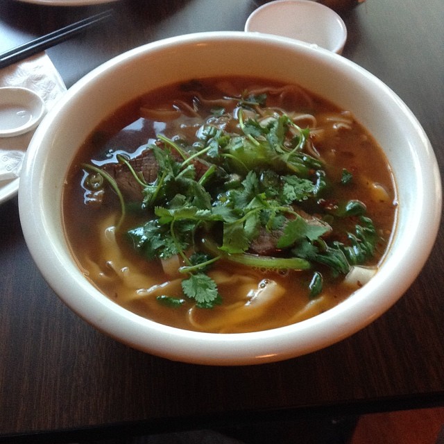 there is a bowl of soup with noodles, meat and greens