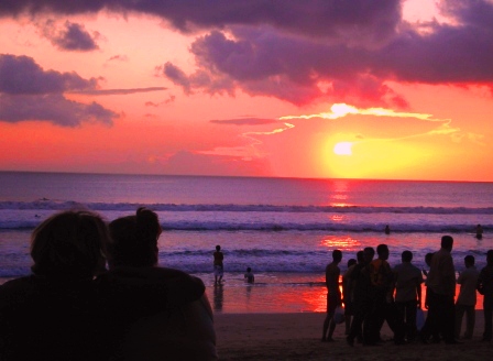 several people standing on the beach watching the sun go down